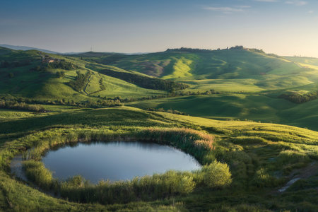 Small lake in the rolling hills of the Crete Senesi at sunset. Spring landscape in Monte Sante Marie, Asciano, Province of Siena, Tuscany region, Italyの写真素材