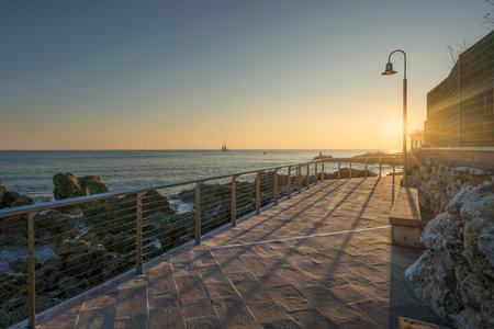 The seafront promenade of Castiglioncello at sunset and a boat in the sea. Province of Livorno, Tuscany region, Italyの写真素材