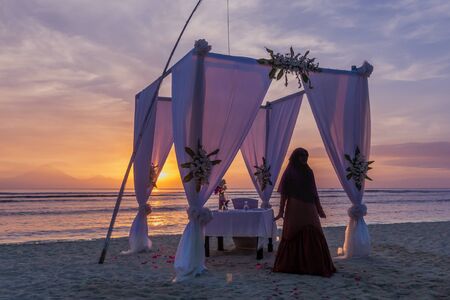Muslim woman in a long brown dress standing in front of a luxory dinner table on the beach in the sunset, april 24, 2018, Gili Trawangan, Indonesiaのeditorial素材
