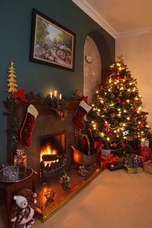 Celebrating Christmas in the home with a Christmas tree, gifts and a nice warm fire.のeditorial素材