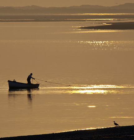 A fisherman hauling in his nets at sunset on the coast near Caernarfon in Gwynedd in Wales のeditorial素材