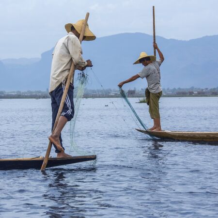 Leg rowing fisherman in the dawn light on Inle Lake in Shan State, Myanmar  Burma  This unique style of rowing evolved because the shallow lake bottom is covered by reeds and plants making it difficult to see the fish while sitting  Standing gives a betteのeditorial素材