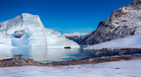 Adventure tourists near an iceberg grounded in a shallow inlet of Franz Joseph Fjord in eastern...