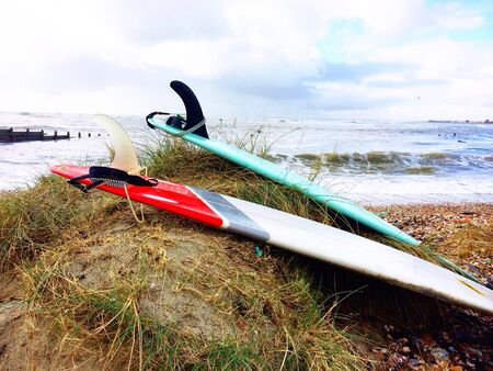 Two surfboards laying on a grassy sand dune at a surf beach