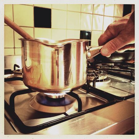 Male hand holding a stainless steel saucepan over a gas flame on a cookerの素材