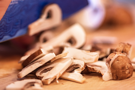 Sliced mushrooms on wood cutting board, blue knife blade.