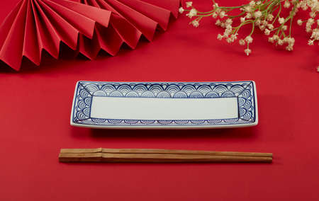 Red folding fans with small flowers, auspicious cloud pattern long plate and chopsticks on red backgroundの写真素材