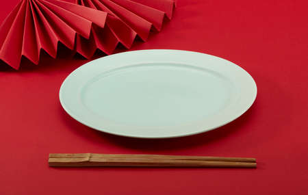 Wooden chopsticks, red folding fans and light green oval plate on red backgroundの写真素材