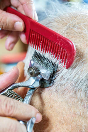 The barber is cutting the hair of an old man with gray hair