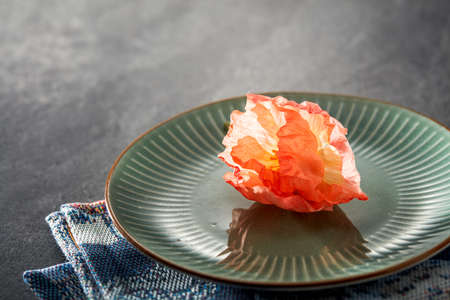A red flower placed on a green dinner plate on a marble tile background
