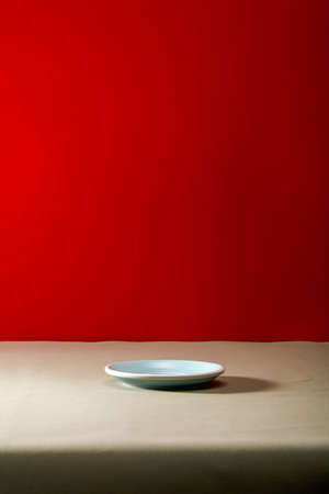 Empty saucer on olive green leather tablecloth in front of red backgroundの写真素材
