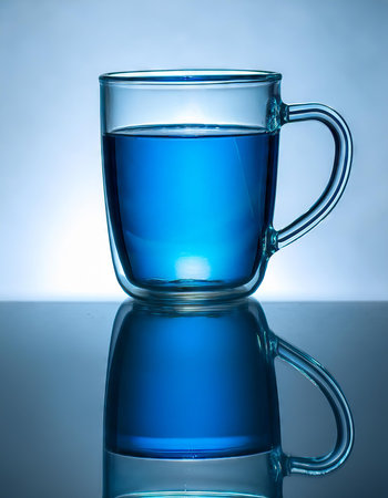 Transparent cup of water on a blue background. Shallow depth of fieldの素材