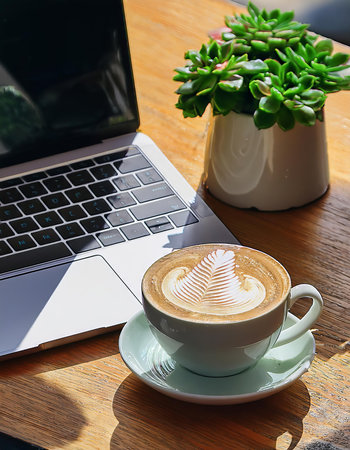 Coffee cup and laptop on wooden table in coffee shop.の素材