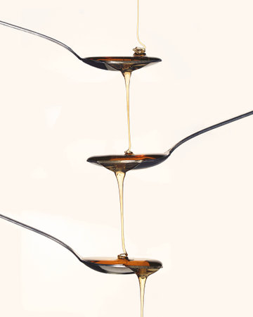 Poured honey overflows from spoon to spoon 
