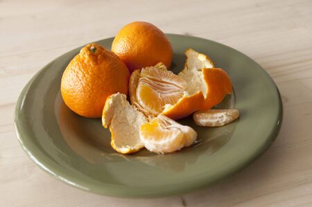 Three tangerines, one of which is peeled, on green plateの写真素材