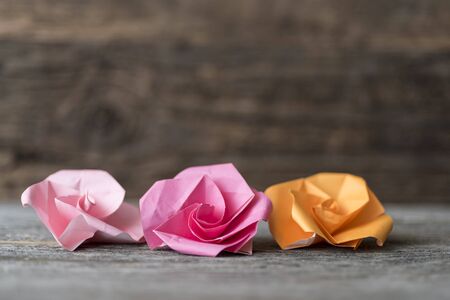 Origami paper flowers in red, pink, and orange for Valentine's Day or springtime against horizontal, rustic, weathered wood backgroundの写真素材