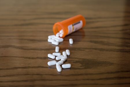 Opioid pills spilled onto a table with orange bottle in the backgroundの写真素材
