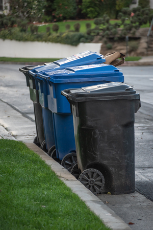 Multi-colored plastic garbage cans full of trash and waiting for pickup on a suburban streetの写真素材