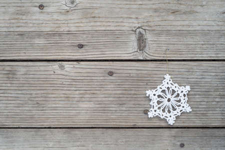 simple, elegant white, woven doily in shape of a snowflake against horizontal gray weathered board...