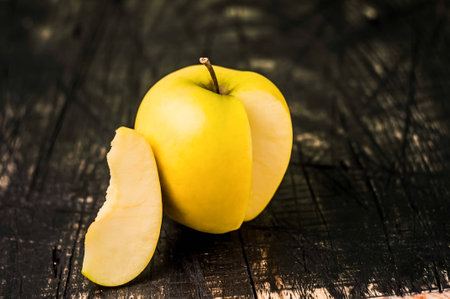 One Juicy yellow apple and piece on the black table. Table with a black wood.の写真素材