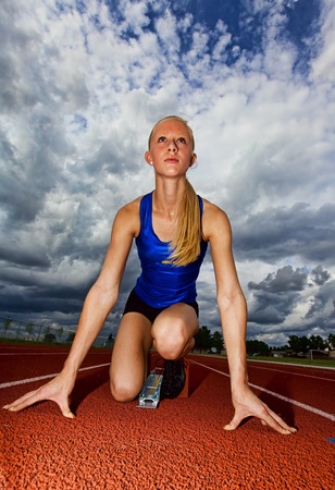 A teenage track athlete in the starting blocks with dramatic sky in the backgroundの写真素材