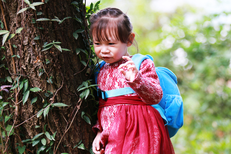 Cute little girl leaning on a tree trunk smilingの写真素材