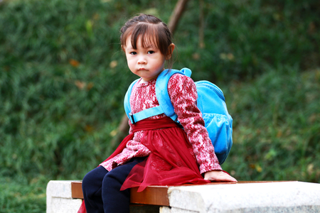 Cute little girl sitting on a stool and biting her lip to look at the cameraの写真素材
