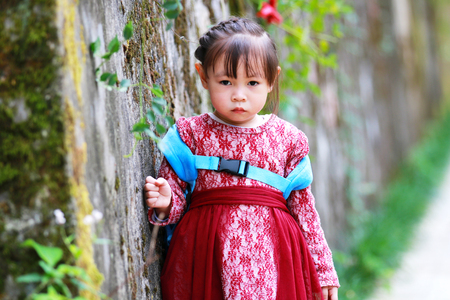Cute little girl leaning against the wall looking into the cameraの写真素材