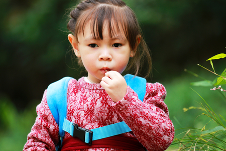 Cute little girl sitting on the grass in the park with grass in her mouthの写真素材