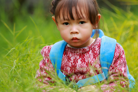 Little girl sitting on the grass staring at the cameraの写真素材