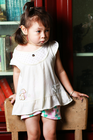 Cute little girl standing on a chair and holding a chair backの写真素材