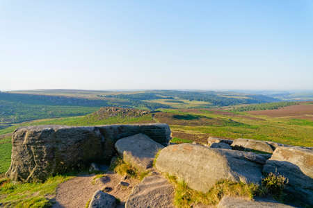 Over large gritstone boulders on top of Higger Tor to the ancient Carl Wark Hillfort on a hazy...
