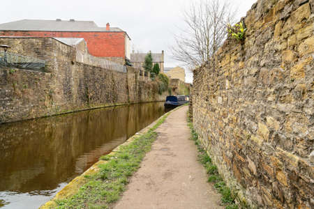 On a dull day the Leeds and Liverpool canal reflects nearby buildings in its surface. In the...