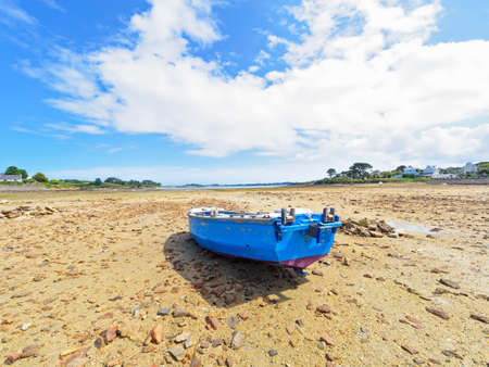 Low tide in Kermengi, Brittany, harbour. A small rowing boat rests on the rocky harbour floor.の写真素材