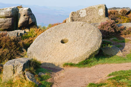 An unfinished millstone sits leaning against gritstone rocks on an autumn morning in Derbyshire