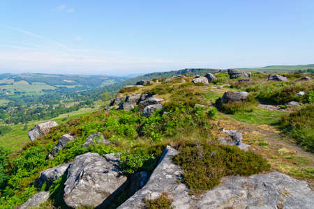 Gritstone boulders of various shapes and sizes are scattered about the steep slopes of Baslow Edge on a misty summer morningの写真素材