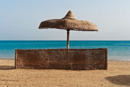 Wicker windbreak and umbrella on a beachの写真素材