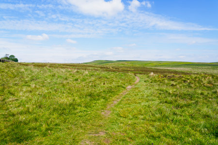 Barely visible winding footpath crosses the Derbyshire hills under a cloudy blue skyの写真素材