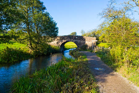 Old stone arched bridge over the Cromford canal on a cloudless autumn morning in Derbyshire.