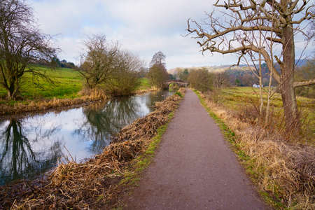 Looking down the Cromford Canal towpath towards an old stone arched bridge on a cold winter day.