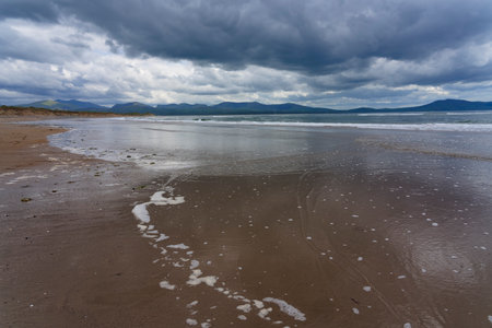 Dark grey clouds roll across Llanddwyn bay as the incoming tide washes up the beach.の写真素材