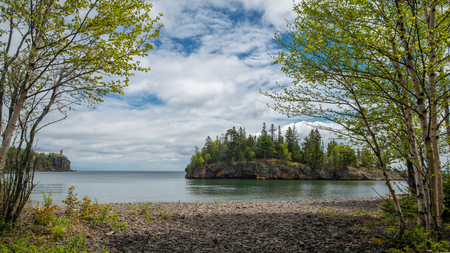 birch grow on the rocky shoreline of lake superior, ellingson island and split rock lighthouse beyond, minnesota.の写真素材
