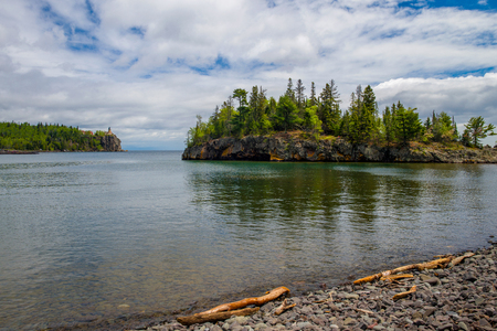 driftwood on the rocky shoreline of lake superior, ellingson island and split rock lighthouse beyond, minnesota.の写真素材