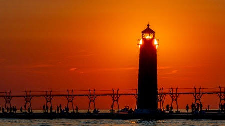 The lighthouse pier at Grand Haven, Michigan, shown in silhouette as the sun sets over Lake Michiganの写真素材