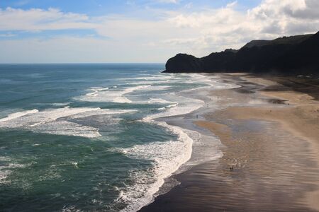 People walking on Beach with surf waves rolling in piha, new zealandの写真素材