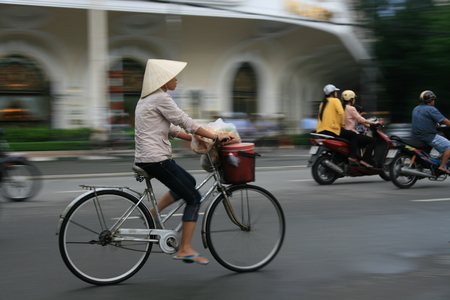 Woman cycling on busy Hanoi Road with traditional Vietnamese hatのeditorial素材