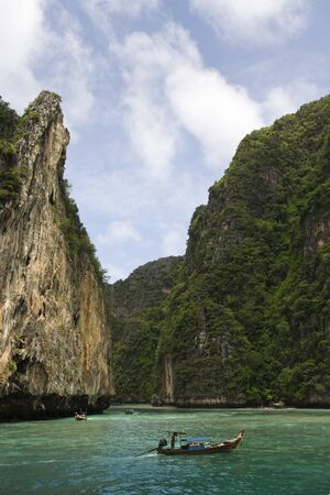 Long Tail Boat passing between dramatic tropical sea cliffs, Maya Beach, Ko Phi Phi Lei, Thailandの写真素材