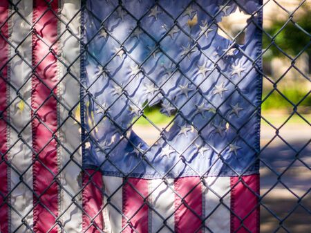 Tattered American flag hanging on chainlink fenceの写真素材