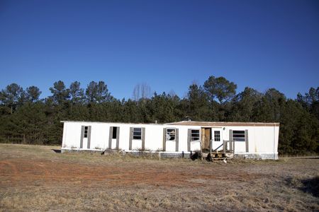 An ugly, wrecked and abandoned mobile home sits alone in an empty field under a brillant blue sky. Good image to use for decay, abandonment, poverty, or evacuation.の写真素材