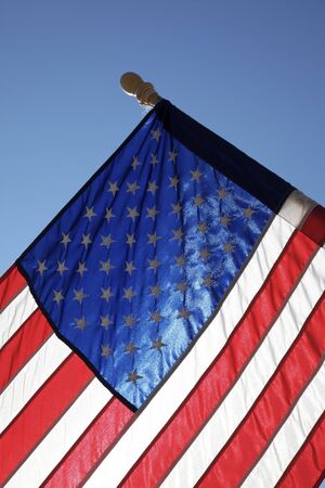 The American flag hangs proudly with a blue sky background on Main Street in Hometown America.の写真素材